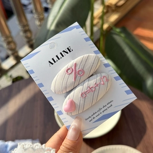 Close-up of light blue striped hair clips with pink embroidery and heart pendant