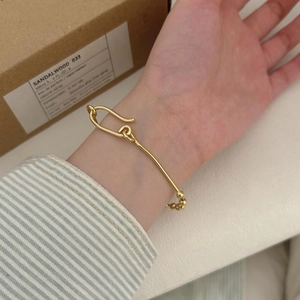Close-up of gold beaded bracelet with paperclip clasp worn by a model in warm lighting