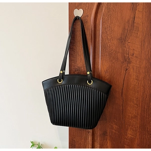 Detail of black pleated shell bag with golden metal rings hanging on a rustic wooden door