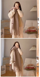 Close-up of khaki tassel scarf shown in a cozy home setting by a lifestyle model