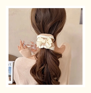 Detail of cream bow scrunchie showing knitted texture and satin ribbon on a ponytail