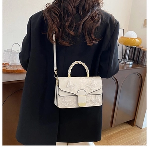 Détail d'un sac à main brodé blanc avec papillons 3D porté par un mannequin en blazer