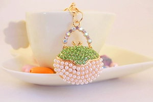 Detail of green crystal and pearl studded handbag keychain in polished gold metal