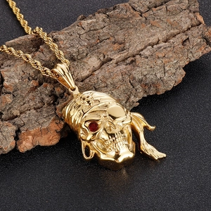 Pendentif tête de mort pirate vintage doré avec œil en pierre rouge sur fond en bois
