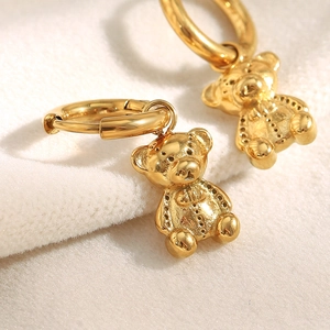 Detailed macro view of 18K gold plated teddy bear charm earrings on white plush fabric