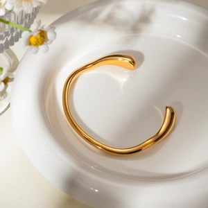 Polished minimalist 18k gold plated stainless steel irregular open bangle on ceramic dish