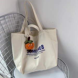 Detail of cream canvas tote bag with blue lettering and a cute plush persimmon charm