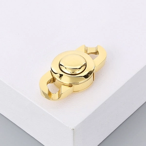 Close-up of a polished golden stainless steel chain clasp on a white geometric stand