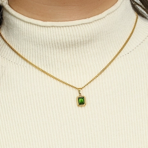 Elegant gold necklace with square green emerald pendant on a white textured sweater