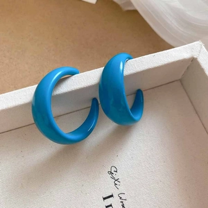 Close-up of vibrant blue C-shaped acrylic hoop earrings on a white textured display box