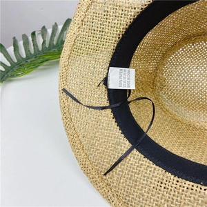 Detail view of straw fedora hat interior showing black sweatband and 100% paper material label
