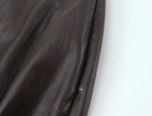 Dettaglio macro della texture in finta pelle marrone scuro e pieghe del tessuto sulla gonna