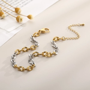 Detail of two-tone gold and silver chain anklet with lobster clasp on beige background