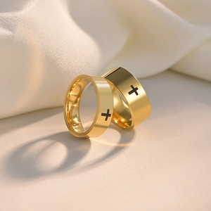 Detail showing a pair of gold stainless steel cross rings on beige silk fabric