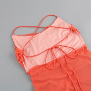 Detail of coral mesh dress featuring thin straps, lace-up design, and ruched texture