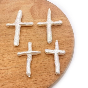 Detailed view of four white baroque freshwater pearl cross beads on a wooden tray