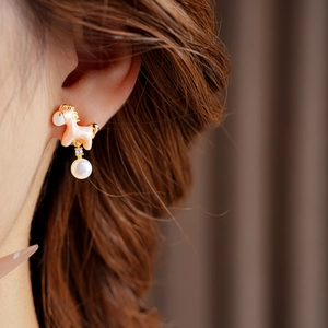 Close-up of golden horse earrings with pink enamel and pearl on female ear