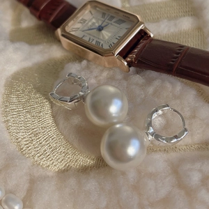 Detail of silver huggie earrings with white pearls on a soft beige fabric background