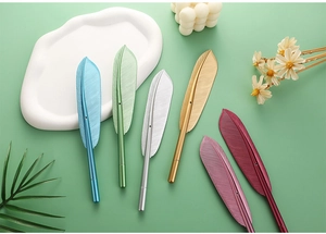 Flat lay of colorful metallic feather pens in blue, gold, and pink on a green background