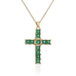 Macro shot of gold-plated cross pendant with green square zircons on white background