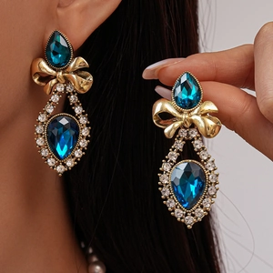 Macro detail of vintage bow earrings with navy blue teardrop gemstones and crystal accents