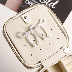 Detail of handmade pearl bow earrings with large drop pearls on a white jewelry stand