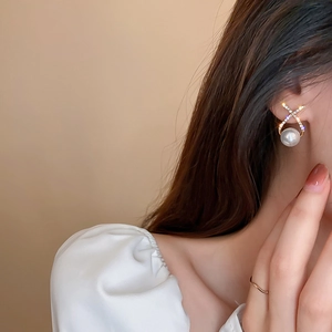Close-up of X-shaped gold stud earring with micro-diamonds and a large white pearl