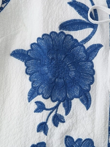 Close-up of blue floral embroidery on white pleated fabric showing intricate stitch detail