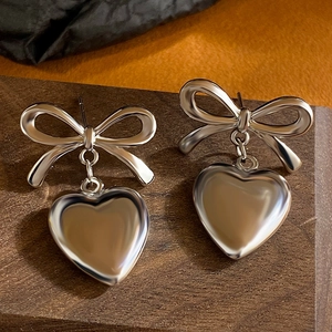 Macro shot of silver bow stud earrings with heart pendants on dark wood and fabric