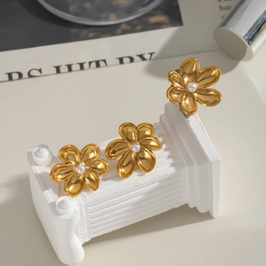 Elegant gold camellia flower stud earrings with central white pearl on a display stand