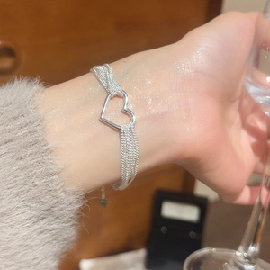 Close-up of a silver multi-layered chain bracelet with a hollow heart charm on a wrist