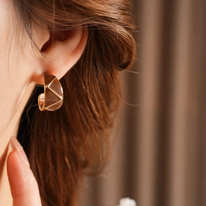 Close-up of a model wearing vintage gold geometric C-shaped earrings with enamel texture