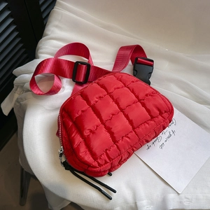 Close-up of red quilted nylon waist bag with adjustable strap on white fabric background
