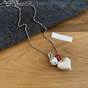 Silver bead necklace with heart pendant and red accents on wooden surface