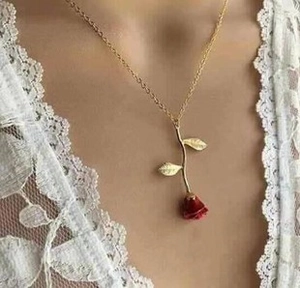 Detailed close-up of a red rose pendant necklace with a golden chain worn on a neck