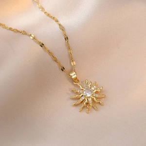 Golden sunburst pendant necklace with central zircon on elegant silk fabric background