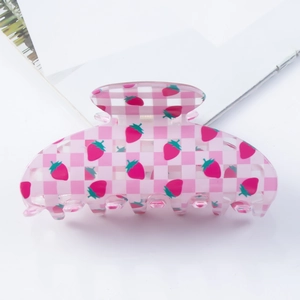 Detailed view of large pink checkered strawberry hair claw clip on magazine background