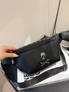 Minimalist black leather waist bag with skull emblem and studded detail on a book