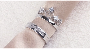 Close-up of silver crown and cross couple rings with sparkling stones on soft fabric