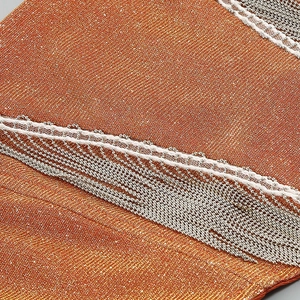 Detailed macro view of orange metallic fabric with white lace and silver beaded fringe