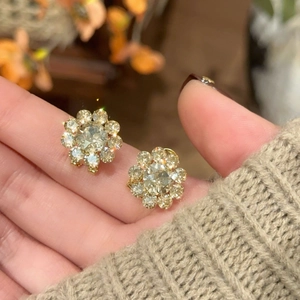 Close-up of gold plated flower stud earrings with sparkling crystals held in hand