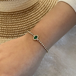 Gros plan d'un élégant bracelet en zircon vert émeraude porté au poignet avec chaîne dorée
