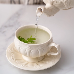 Detailed view of pouring tea into a vintage cream ceramic cup with embossed relief
