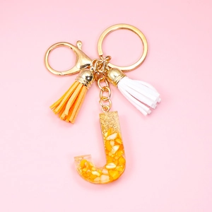 Detailed close-up of resin letter J keychain with yellow corn fillings and orange tassels
