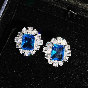 Macro shot of emerald-cut blue gemstone earrings with halo diamonds and prong setting