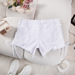 Dettaglio di pantaloncini in denim bianco strappato con lacci laterali su un divano