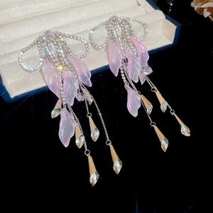 Detail of tassel earrings with pink petals, crystal bow, and silver chains on black velvet