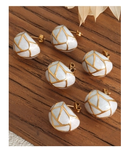 Macro detail of vintage geometric titanium steel earrings with white enamel and gold texture