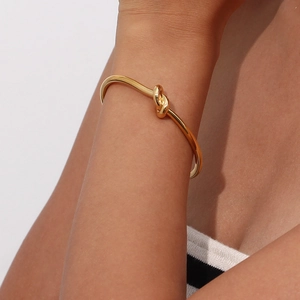 Close-up of a model wearing a polished 18K gold plated minimalist knot open cuff bracelet