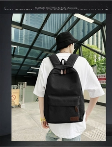 Detail of black canvas backpack with front flap pocket and brown leather logo patch